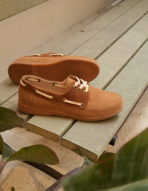 Par de mocasines estilo apache color latte con cordones blancos sobre una superficie de listones de madera. Calzado plano de moda ética.