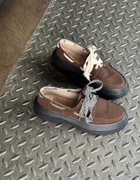 Par de Mocasines Apache Chunky Café de Animalista sobre escalera metálica, mostrando la opción de cordones intercambiables. Zapatos veganos de plataforma track y diseño en Medelln