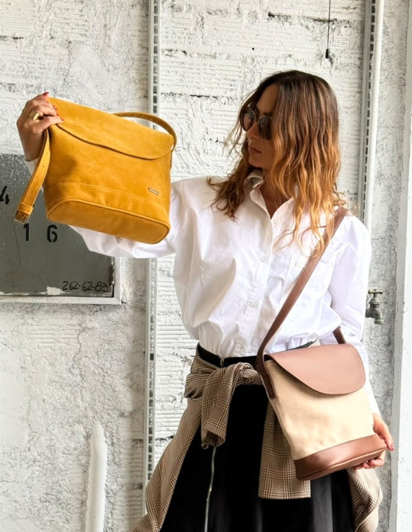 Mujer vistiendo camisa blanca y falda negra, luciendo el Bolso Cylinder estructurado color mostaza de Animalista. Accesorio de moda vegana.