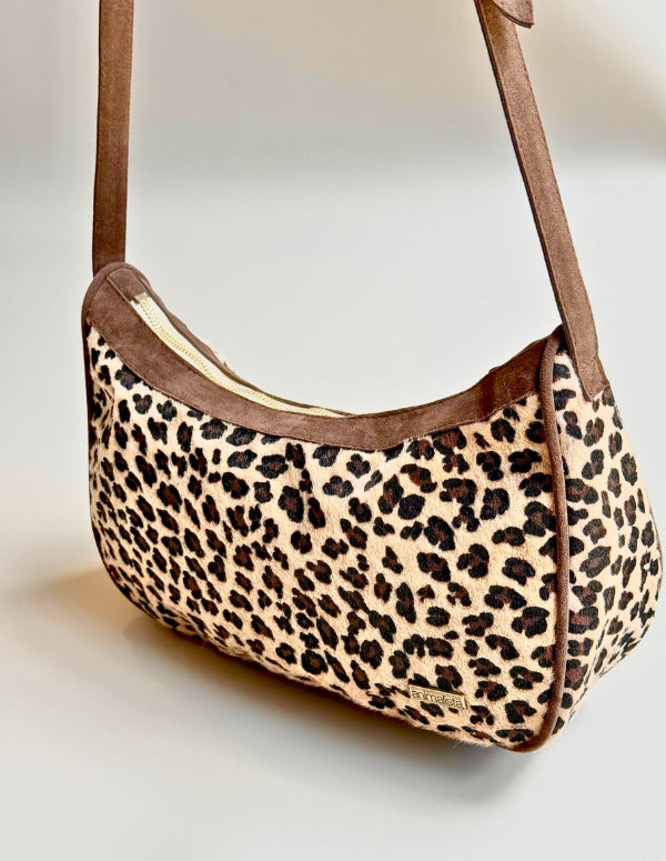 Vista lateral de cartera estilo hobo con estampado de leopardo y cargadera café. Fabricado sin materiales de origen animal.
