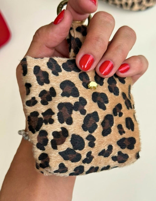 Mano sosteniendo un charm tipo monedero pequeño con estampado animal print leopardo. Llavero accesorio vegano y libre de crueldad.