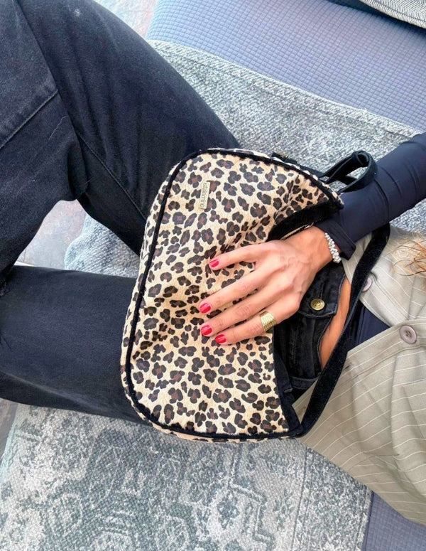 Mujer luciendo un bolso cruzado tipo hobo estampado leopardo con bordes negros. Diseño local hecho a mano en Medellín.