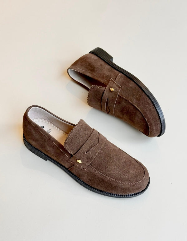 Fotografía superior directa de dos mocasines idénticos marrones de gamuza tipo penny loafer Animalista sobre un fondo blanco.