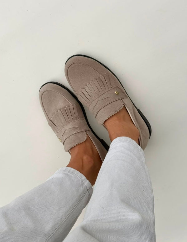 Vista superior de zapatos mocasines planos color arena combinados con pantalón blanco.