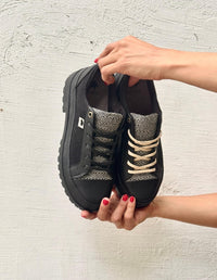 Manos sosteniendo un par de tenis negros para mujer de suela alta plataforma con detalles texturizados. Calzado urbano de moda consciente hecho en Colombia.