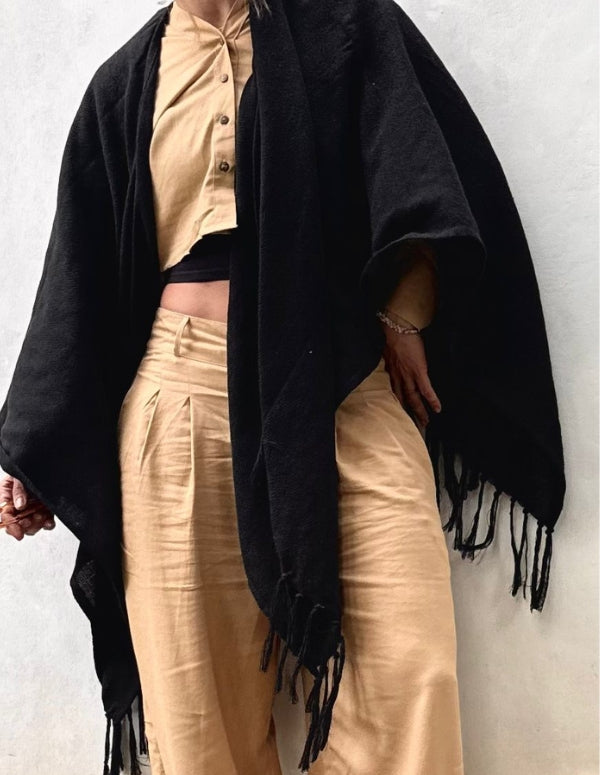 Modelo luciendo el Poncho Negro con flecos de Animalista sobre conjunto beige. Ropa de mujer sostenible, diseño bohemio y moda local.