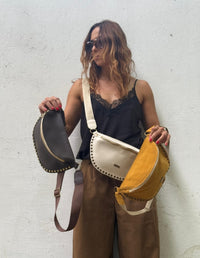 Mujer modelando tres fanny packs o canguros con taches metálicos en colores negro, beige y mostaza. Accesorio manos libres de moda vegana hecho en Colombia.