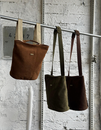 Tres bolsos casuales modelo Slow en colores miel, verde oliva y café oscuro colgados de una barra metálica   . Bolsos veganos Animalista.