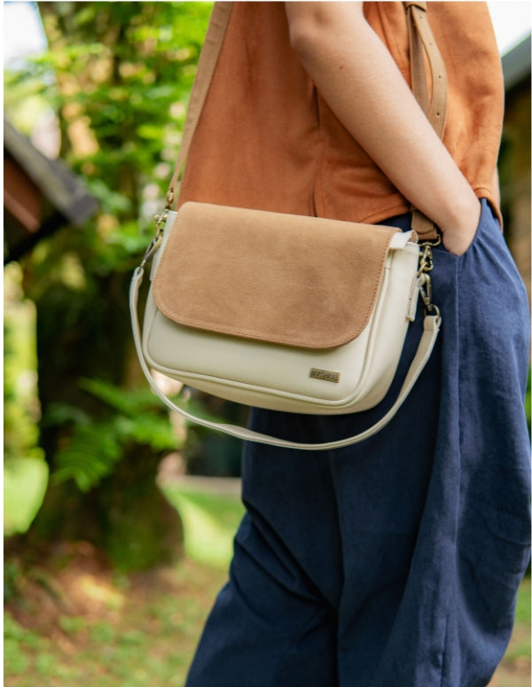 Mujer luciendo un bolso midi estilo bandolera color beige con tapa color latte cruzado sobre el cuerpo. Accesorio de moda consciente y vegana hecho en Colombia.