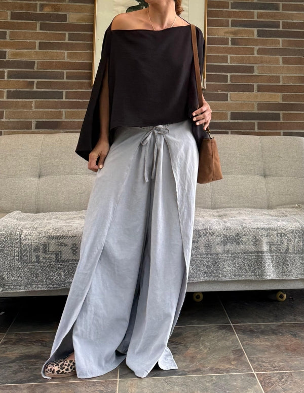 Mujer luciendo un pantalón boho gris claro de silueta amplia con aberturas frontales y top negro. Ropa cómoda de moda consciente hecha en Colombia.