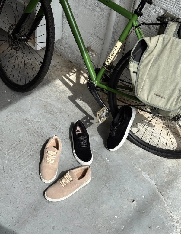 Zapatos estilo pisahuevos color arena descansando junto a una bicicleta urbana. Estilo de vida casual y moda ética masculina.