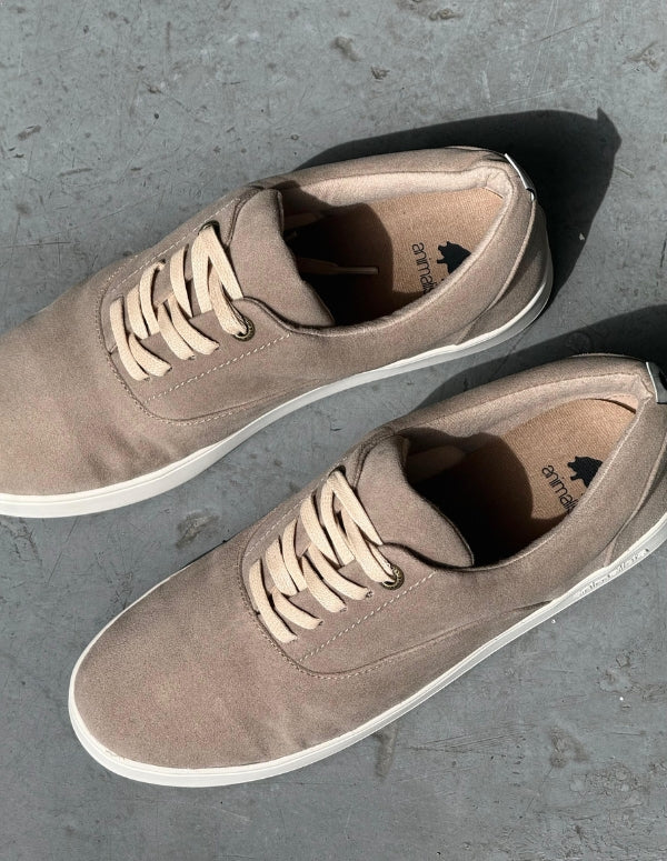 Vista superior de par de zapatos casuales masculinos color arena sobre superficie de concreto.