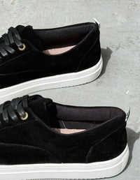 Perfil de zapatos casuales masculinos color negro destacando la suela plana blanca y las costuras.