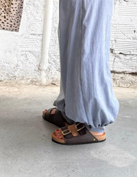 Mujer vistiendo pantalones anchos celestes y top blanco, luciendo las Sandalias Mar Café Oscuro de Animalista