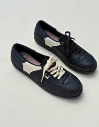 Par de tenis casuales color negro para mujer con paneles laterales y cordones en contraste color crema. Calzado vegano hecho en Colombia.