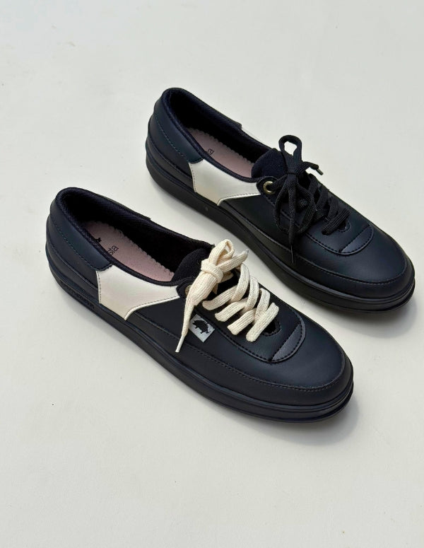 Par de tenis casuales color negro para mujer con paneles laterales y cordones en contraste color crema. Calzado vegano hecho en Colombia.